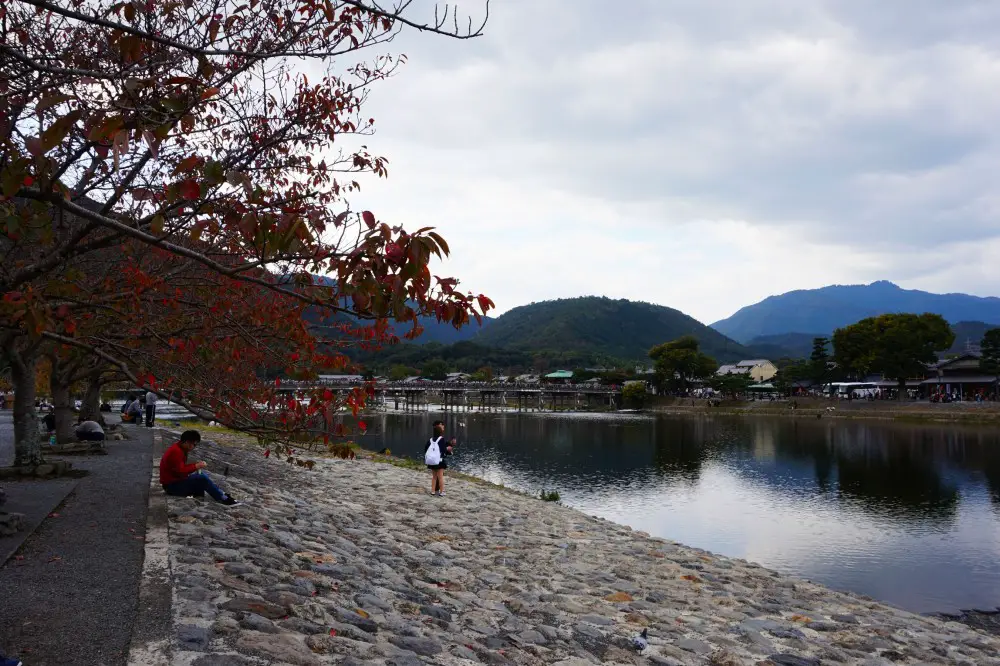 autumn foilage on the bank of river at Arashiyama, with Togetsukyo Bridge and Arashiyama in the background | Laugh Travel Eat