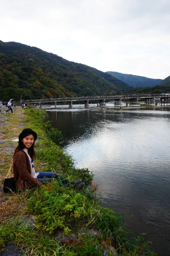 Posing along the bank of river in front of Togetsukyo Bridge in Arashiyama, Kyoto, Japan | Laugh Travel Eat